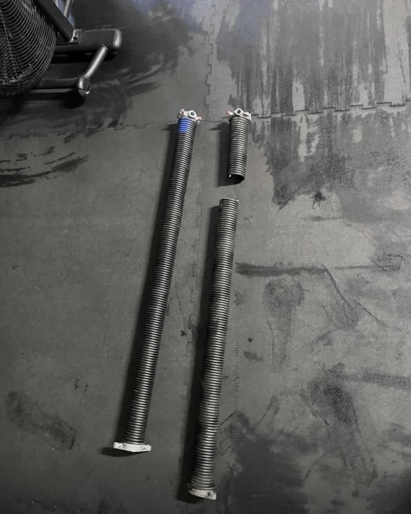 Two broken garage door torsion springs removed from a door, one snapped in two
