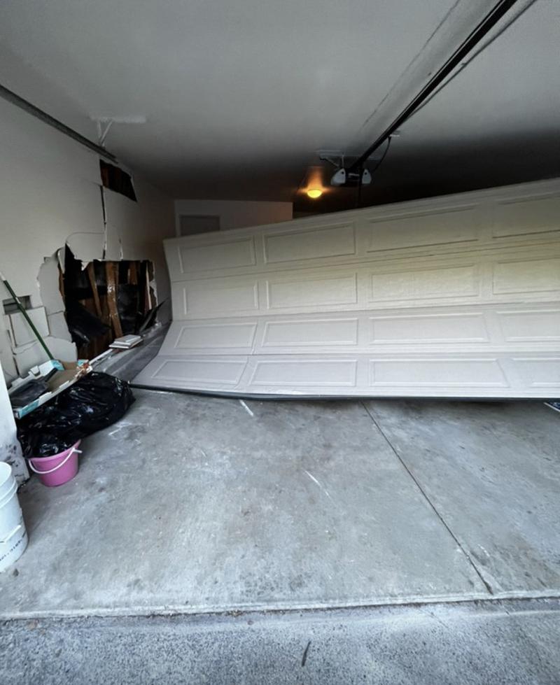 Garage door fallen off its tracks and leaning inside a damaged garage