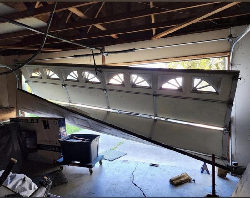 Garage door with arched windows hanging off its tracks at a steep angle inside a garage