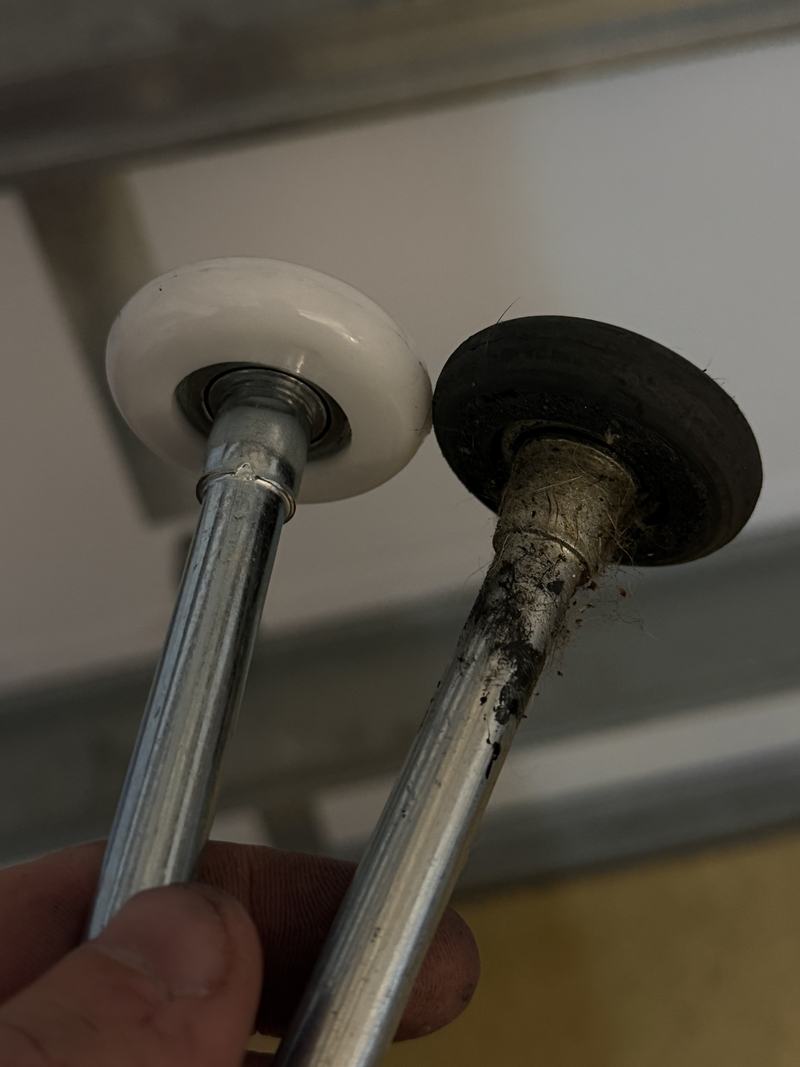 A new white sealed-bearing nylon garage door roller held next to a worn, dirty old roller